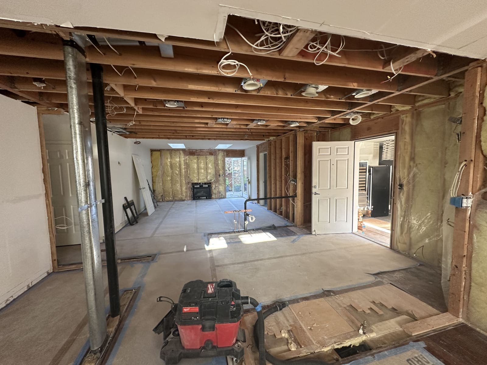A kitchen gutted down to the ceiling joists and studs, with wiring, insulation and plumbing stubs exposed